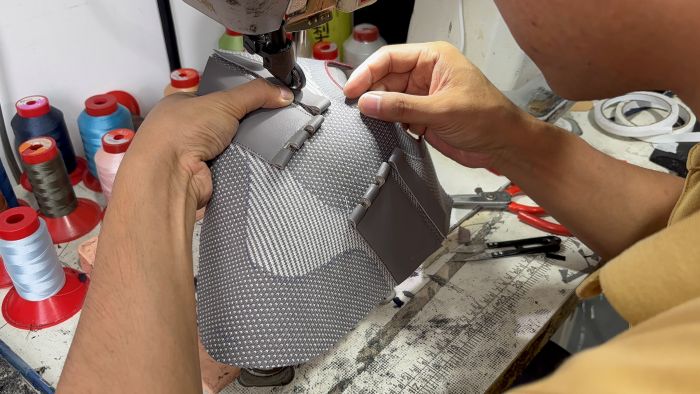 Close-up of a worker's hands precisely guiding a grey knit sneaker upper through an industrial sewing machine, highlighting skilled craftsmanship and attention to detail during custom footwear manufacturing