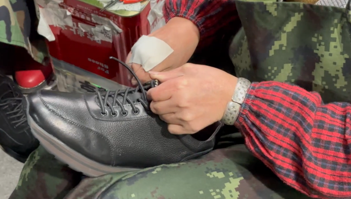 Close-up of a factory worker tying shoelaces on a finished black leather shoe during final quality inspection and packaging, ensuring attention to detail before wholesale shipment.