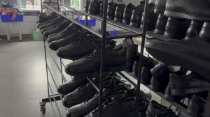 Multi-tier metal display racks stocked with large quantities of black leather dress shoes in the manufacturing facility, demonstrating strong production capacity and reliable OEM footwear inventory management